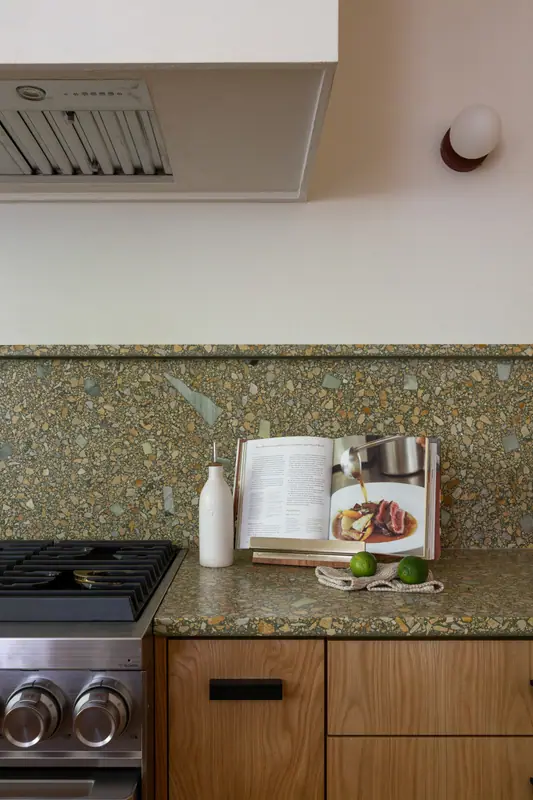 The stainless hood liner and full-height quartz backsplash above the range, with a cookbook on the counter