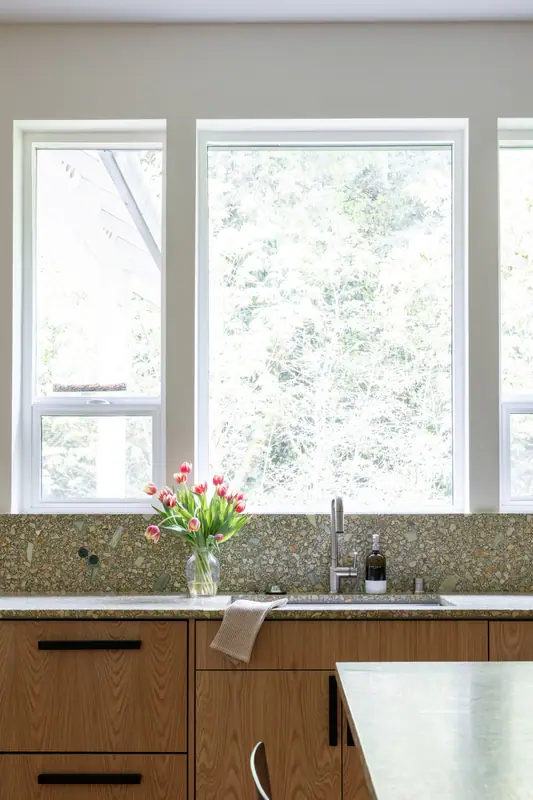 The undermount sink and black faucet under the window, with tulips and the quartz backsplash