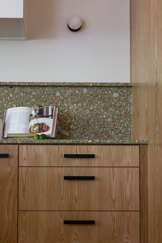 Detail of the terrazzo-look quartz counter and backsplash against the white oak drawer fronts and black bar pulls