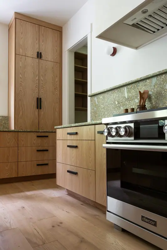 The range corner: stainless range, plaster hood, the pantry doorway with its oak shelving and a built-in microwave at the right