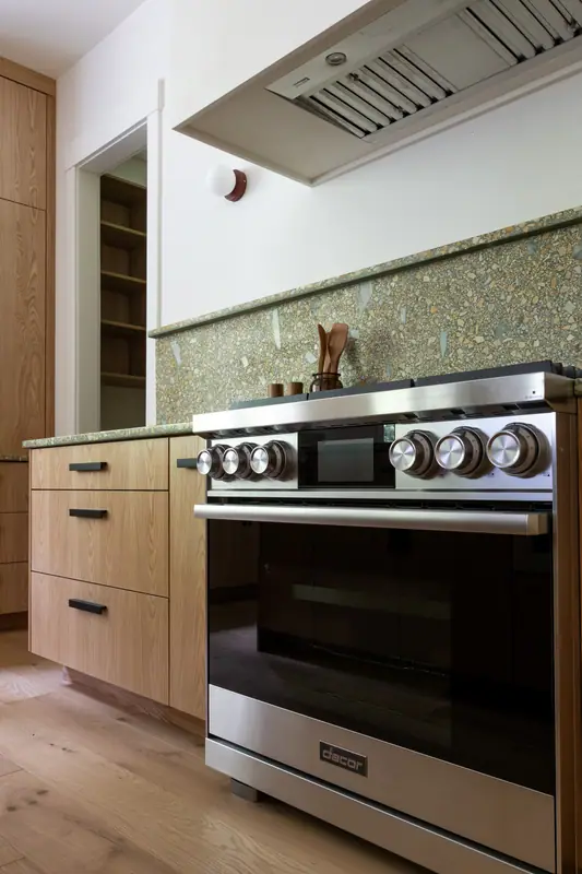 The stainless pro-style gas range head-on, with the hood liner above and full-height oak cabinetry alongside