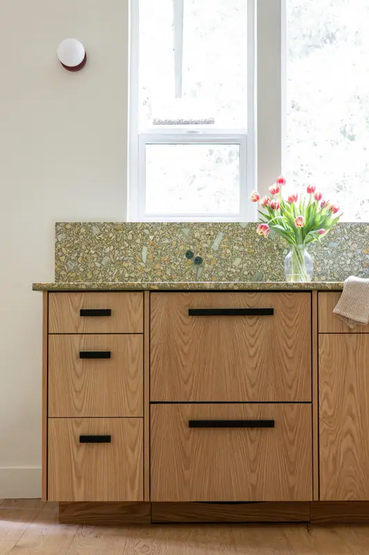 The base cabinets under the window with tulips on the quartz counter and matte black bar pulls