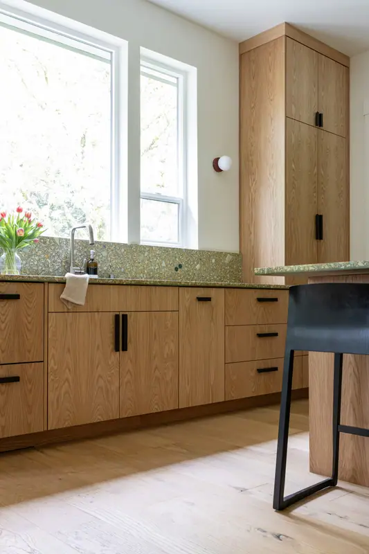 The sink run with the island stool in the foreground and the tall white oak cabinet run beyond