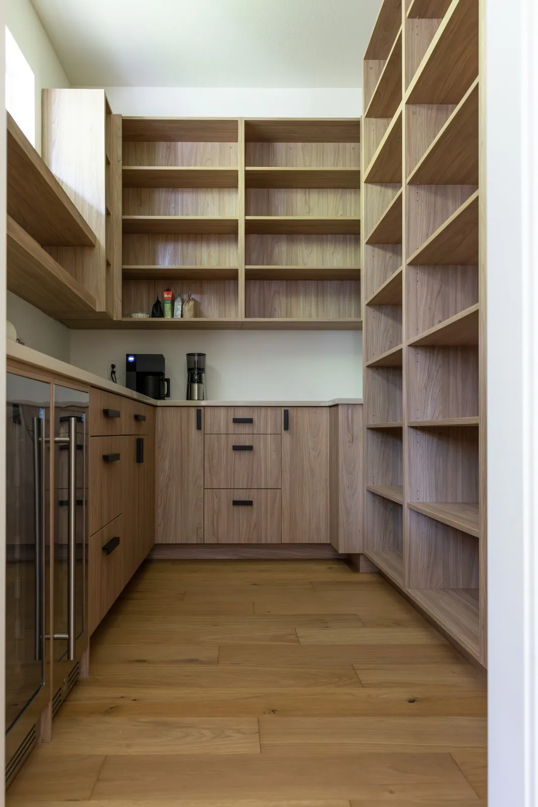 The rebuilt walk-in pantry after remodeling, with custom white oak open shelving on two walls, a counter used as a coffee station and a glass-front wine refrigerator