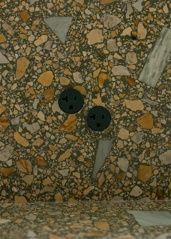 Macro detail of the green terrazzo-look quartz backsplash, with matte black outlets set directly into the stone
