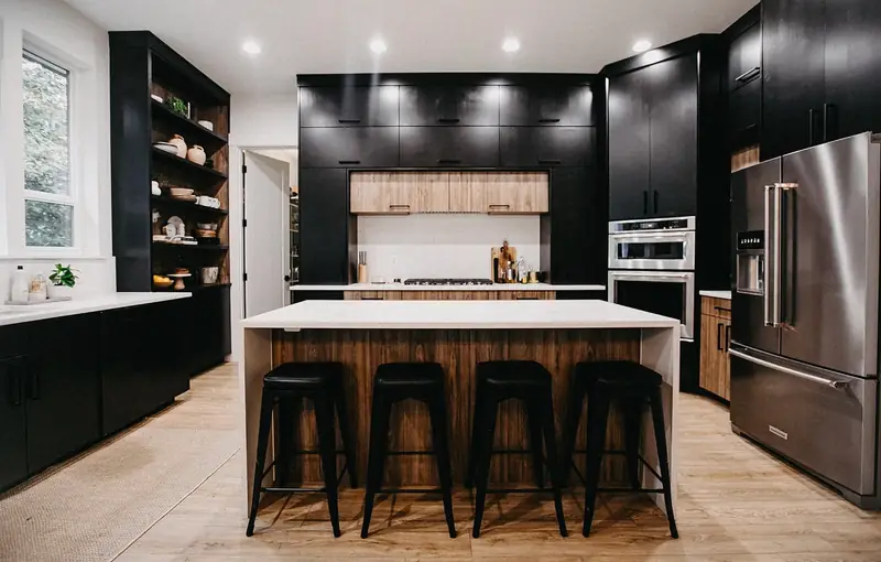 Before the remodel: the original cooking wall head-on, with black upper cabinets, a dark band of cabinetry above the cooktop in place of a hood, wood drawer banks below and a white quartz waterfall island