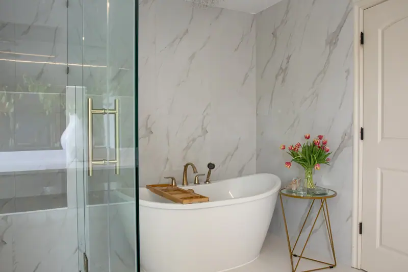 Freestanding soaking tub against marble-look porcelain with the frameless glass steam shower alongside