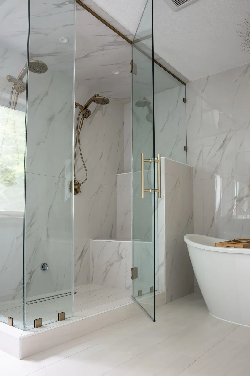 The rebuilt steam shower after remodeling, with a built-in bench, dual heads, a linear drain and frameless glass to the ceiling