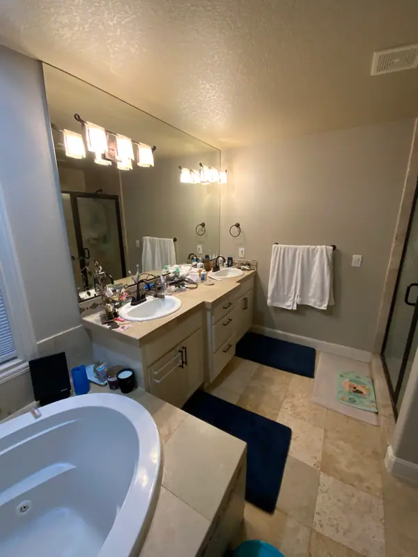 Before the remodel: the cream vanity, its cultured-marble top with two drop-in sinks, and the jetted tub deck at the edge of frame