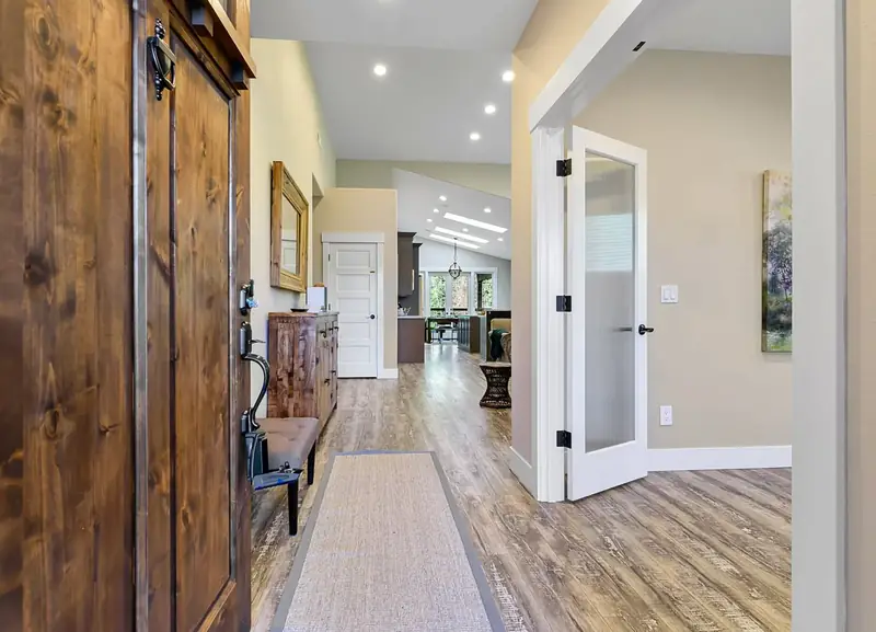 Entry with a knotty alder front door opening onto wide-plank floors and the vaulted great room beyond — Vancouver, WA