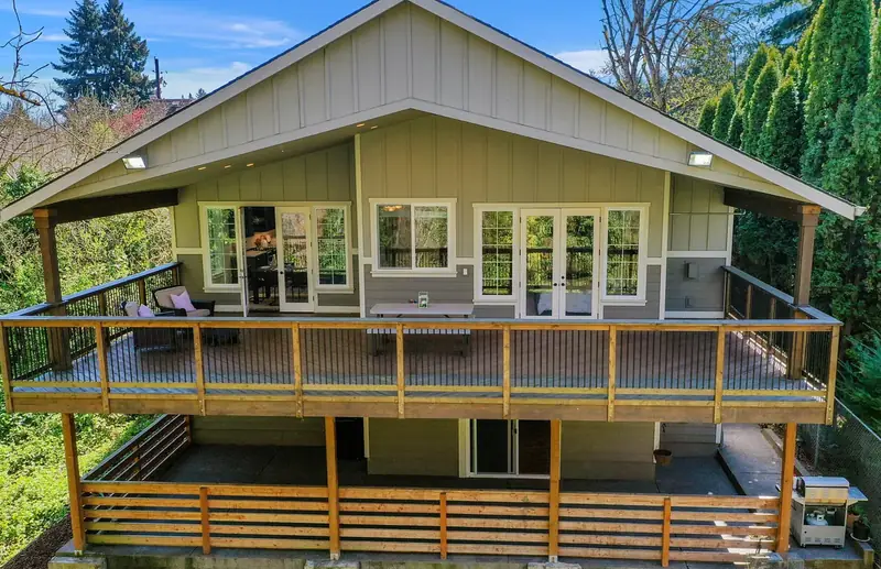 Rear elevation with a deep covered deck above a lower patio, framed by the tree line — Vancouver, WA