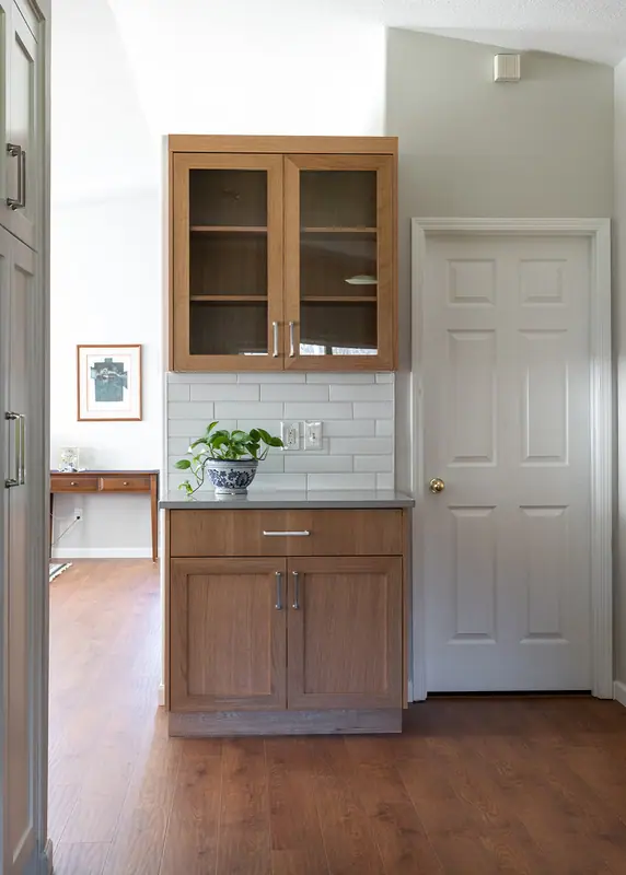 White oak serving hutch with a glass-front upper cabinet beside the laundry room door