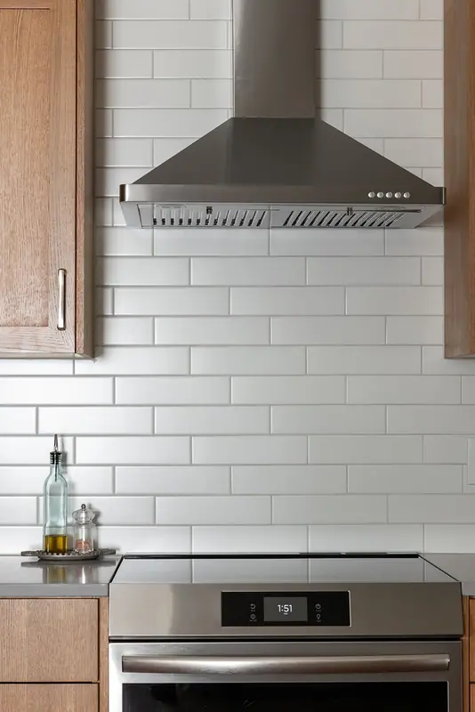 Stainless chimney range hood above the range against white subway tile