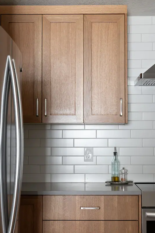 White oak upper cabinet and drawer beside the refrigerator, with subway tile and quartz