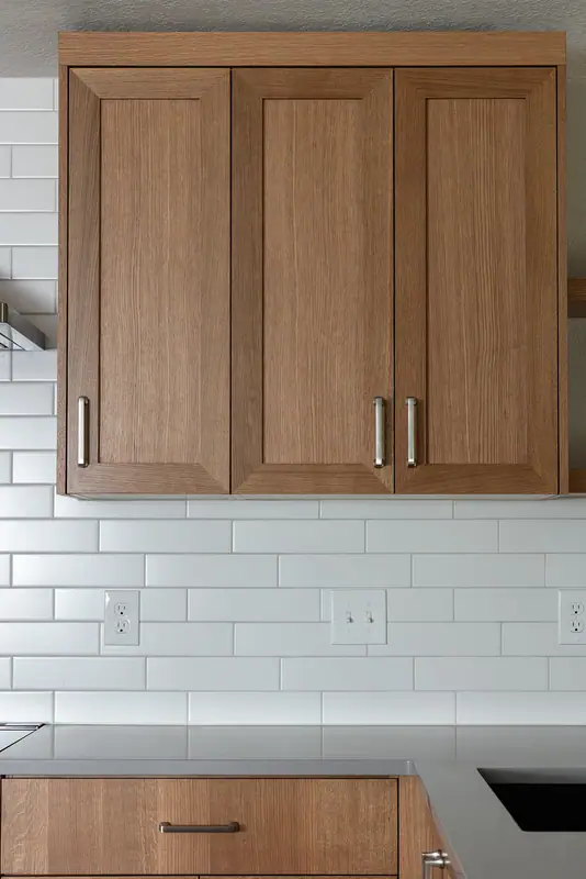 White oak shaker upper cabinets above the white subway tile backsplash and quartz counter