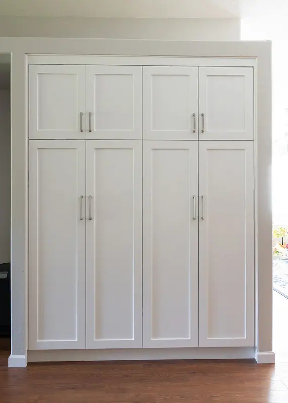 Full-height painted pantry cabinet in paint-grade alder, set into the wall recess beside the kitchen