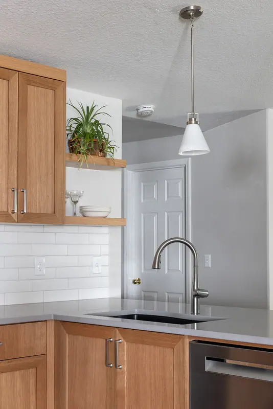 Sink and faucet under a glass pendant, with white oak floating shelves alongside