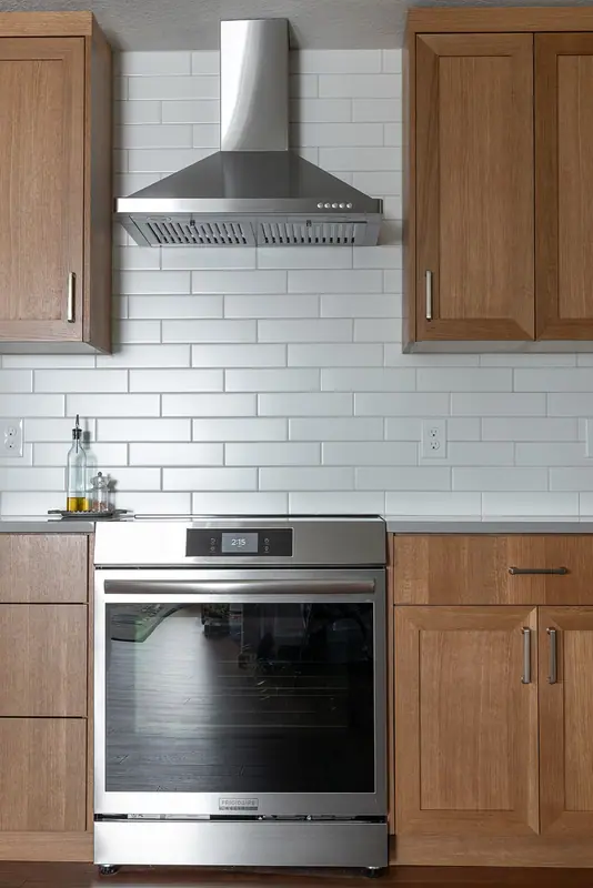 Slide-in range beneath the stainless chimney hood and white subway tile