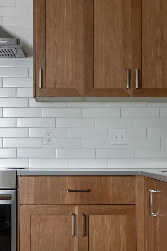 White oak upper cabinets and subway tile above the quartz counter run