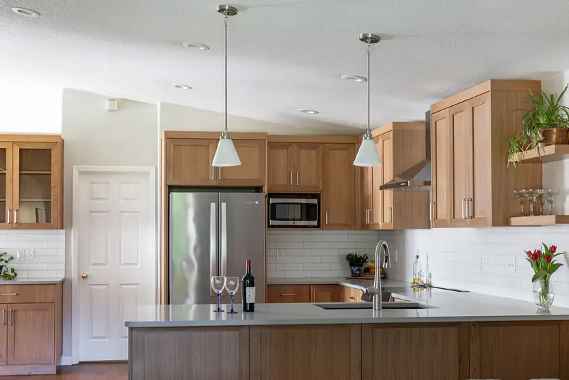 Wide view of the finished kitchen: white pantry, refrigerator, range hood and quartz peninsula