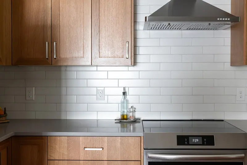 White oak uppers, chimney hood and subway tile above the cooktop