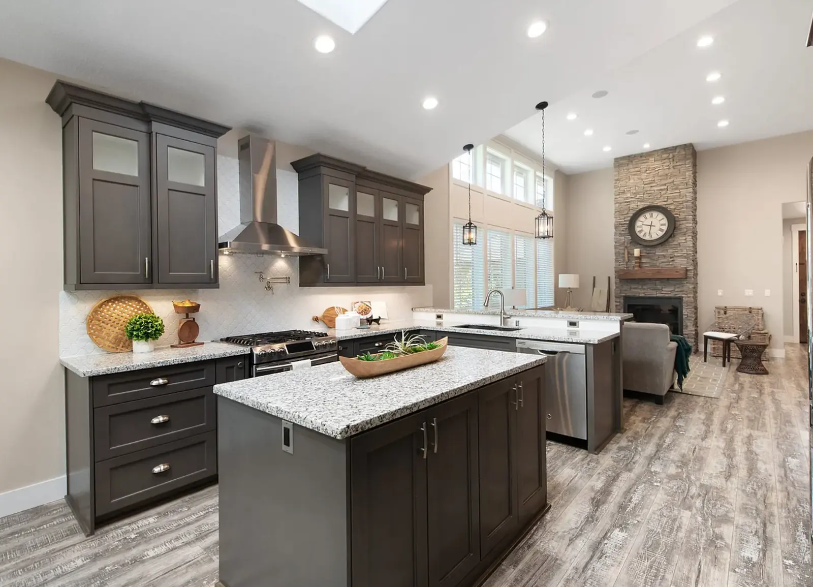 Remodeled open-plan kitchen with light speckled stone countertops, a large island, dark shaker cabinets, and stainless appliances