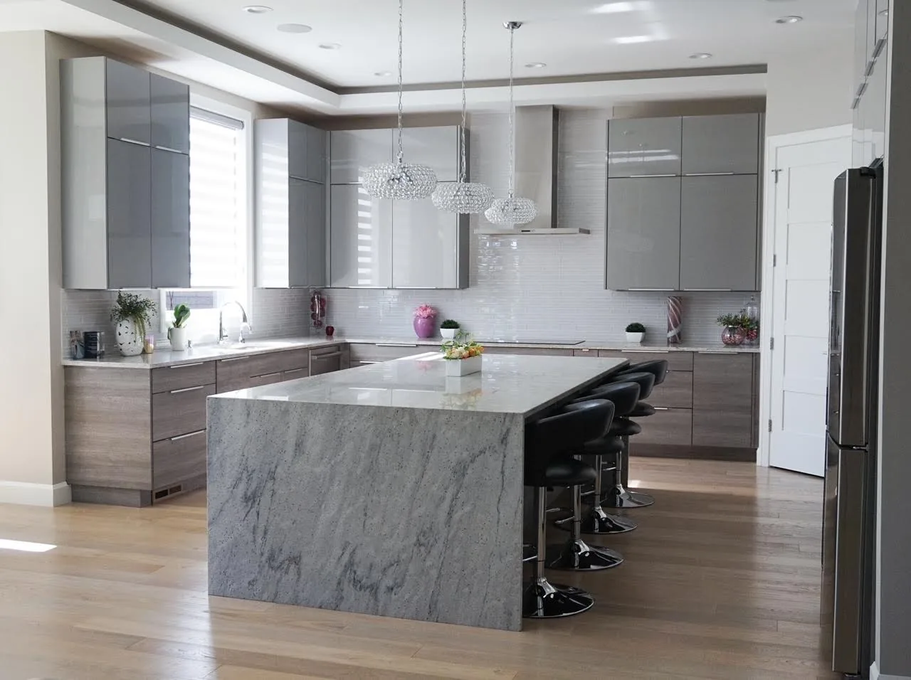 Modern Vancouver, WA kitchen remodel with a waterfall stone island, gloss gray cabinets, and wood-tone lower cabinetry
