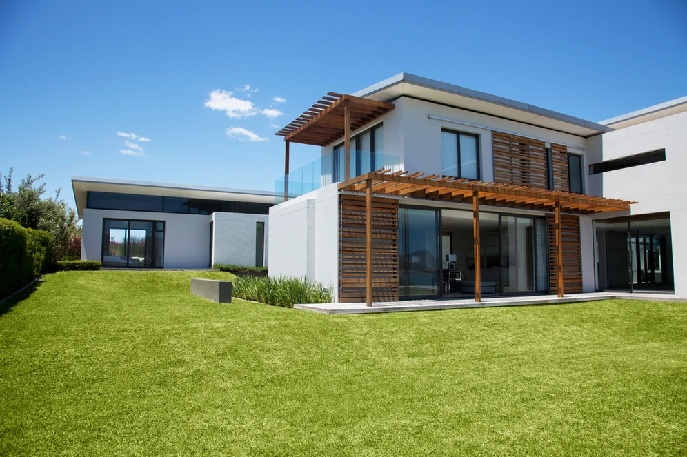 A contemporary house with a lush green lawn and a wooden deck, blending modern design with natural elements.